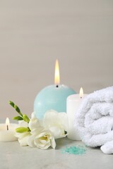 Beautiful spa composition with burning candle, rolled towel and flowers on white table