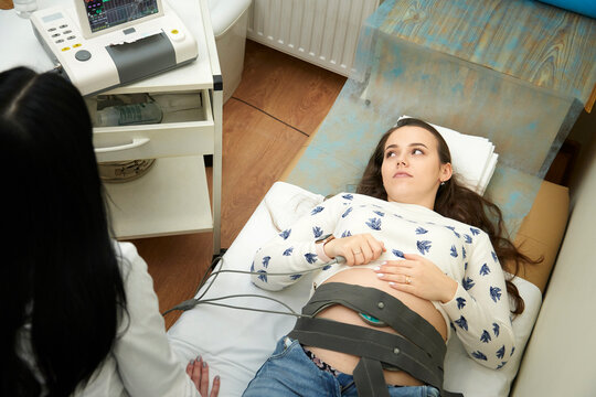 Happy pregnant female visiting her own gynecologist in medical clinic.Doctor examining the baby with stethoscope and ctg graph. Fetal heart monitoring. Cardiotocography.       