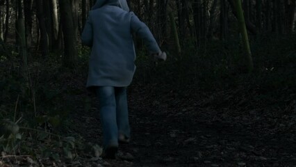 Frightened woman running through dark woodland 