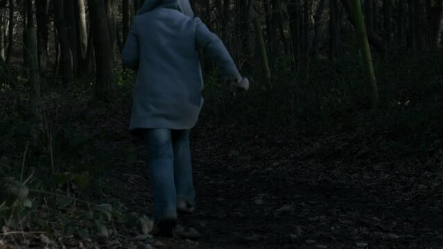 Frightened woman running through dark woodland 