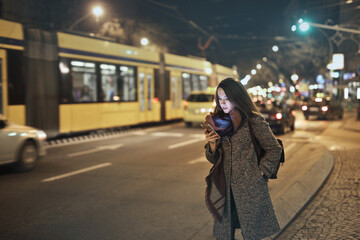 young woman in the city at night while using a smartphone - 558196782