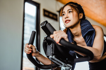 Exercise bike cardio workout at fitness gym.Asian women doing sport biking in the gym for fitness in the morning.Fitness,Gym ,healthy lifestyle concepts.