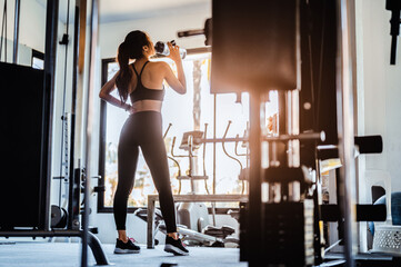 Fototapeta na wymiar Fitness asian woman relaxing after exercise her drinking waters at gym.Relaxing after training.beautiful young woman looking away while standing at Fitness gym.Fitness,bodybuilding,healthy lifestyle.