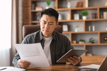 Busy serious concentrated adult japanese businessman analyzes data in documents and tablet, think about online startup