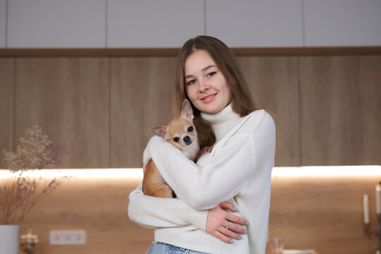 Portrait of young beautiful woman, teenager girl hug with Chihuahua dog, holding on hands little puppy at home at kitchen - Powered by Adobe