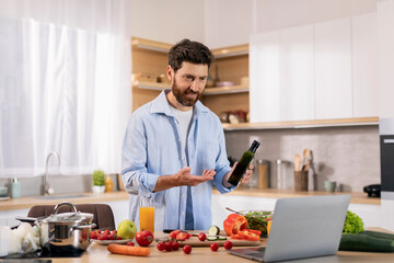 Fototapeta na wymiar Smiling attractive millennial caucasian guy preparing eat at table with vegetables, show oil to computer webcam