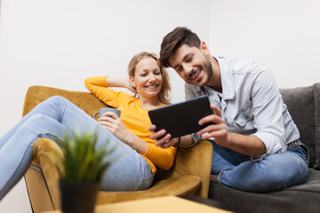 couple at home sitting on a sofa looking at tablet computer. both smiling