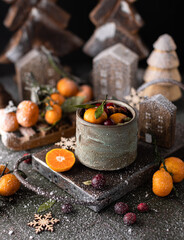 Mulled wine in ceramic glass with spices,oranges,berries,tangerines surrounded by wooden houses miniatures.Winter hot drink.