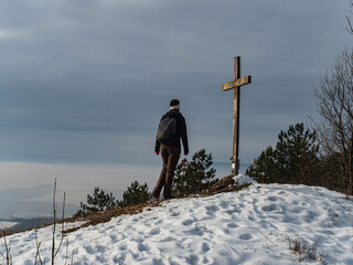 Young faithful woman pilgrim walking to standing at a mountain top cross winter landscape sunshine religion faith hope - obrazy, fototapety, plakaty