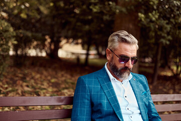 Modern senior businessman resting on a bench in the city on a break from work