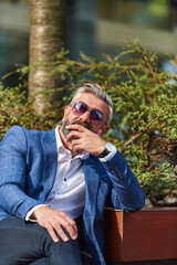 Fototapeta premium Modern senior businessman resting on a bench in the city on a break from work