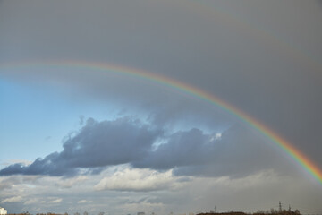 Rainbow in the sky after the rain. Blue sky. White clouds. The sky is visible through the storm clouds. High in the sky. The texture of clouds. It's going to rain soon