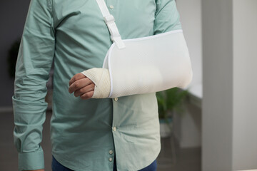 Cropped shot of a man wearing a white bandage and a forearm sling after the surgery on his broken arm. Accident, injury, bone fracture, joint dislocation, treatment concept