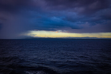 Line of light between dark clouds and water surface during early morning hours near Dominican Republic coastline. Wind power turbines producing clean energy on the shore.