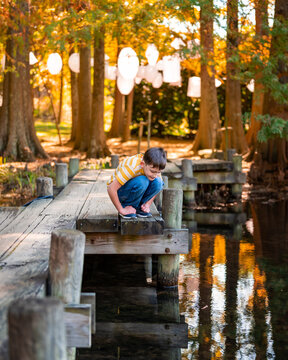 Naklejki A curious boy looking down into a pond from a dock