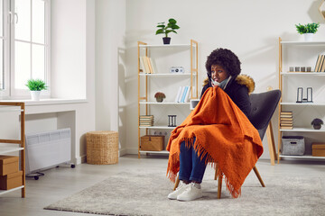 African American woman freezing inside the house in winter. Shivering young Afro American woman in...