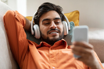 Relaxed arab guy lying on couch with phone and headphones