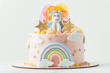 Unicorn cake with pink cream cheese frosting decorated with mastic rainbow, multicolored caramel candies and unicorn shaped figure on top. Birthday cake for a little girl on the white background - Powered by Adobe