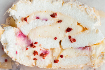Cut of homemade meringue roll decorated with almond flakes and freeze-dried red berries on the white marble background. Meringue roulade with whipped cream on a parchment paper