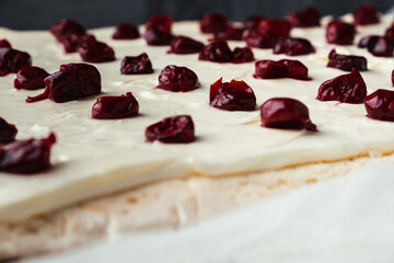 Cut of homemade meringue roll decorated with almond flakes and freeze-dried red cherries on the white marble background. Meringue roulade with whipped cream on a parchment paper
