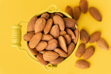 Dried almonds in a yellow bucket on the yellow background. Nuts stacked together randomly with a copy space for a free text. Healthy nutrition concept. Flat lay