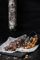 Chocolate salami filled with almonds, hazelnuts and raisins on the black background. Italian sweet sausage shaped dessert sprinkled with powdered sugar. Christmas and New Year festive pastry
