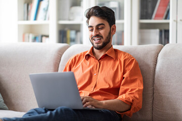 Happy arabic man freelancer working from home, using laptop