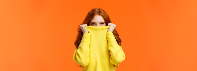 Girl hiding from winter cold in her warm soft sweater. Cute redhead woman pulling collar on nose...