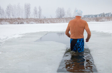 A seasoned strong man plunges into an ice hole, into the icy water in the lake, dipping into the...
