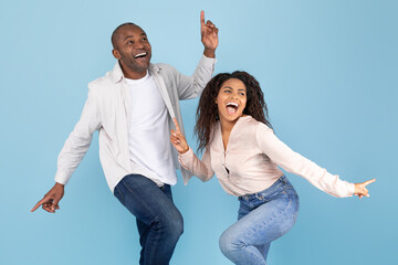 Joyful african american couple dancing and smiling, posing together on blue studio background