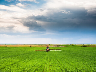 Tractor-applied herbicides, pesticides, and fungicides in wheat fields, farmer protecting crops from pests and weeds
