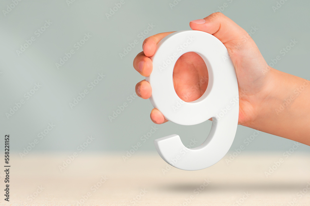 Aufkleber number nine in hand. a hand holds a white number 9 on a blurred background. concept with number nine