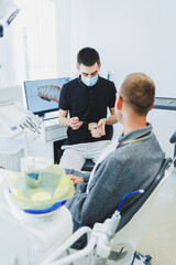 A dentist in a modern dental office tells a patient about dental care. A man sits in a dental chair...