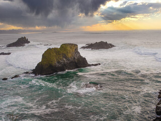 Large stones, boulders in the water. Foamy waves crash against the rocks. Gray stormy sky with an orange sunset. The approach of a storm. Beautiful nature.