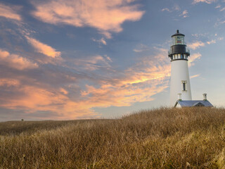 A lighthouse on a high bank under a sky with pink storm clouds. Hilly area with brown withered grass. Beautiful landscape. Tourism, travel, romance, history.