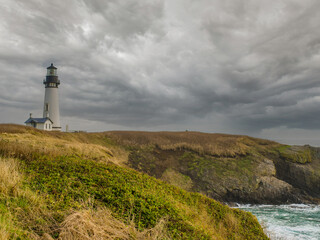 Fototapeta na wymiar lonely lighthouse on a hilly ocean shore. Rocky shore overgrown with grass, gray storm clouds in the sky. History, tourism, recreation, excursions, architecture.