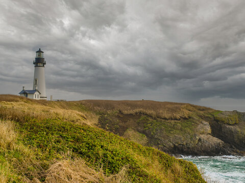 lonely lighthouse on a hilly ocean shore. Rocky shore overgrown with grass, gray storm clouds in the sky. History, tourism, recreation, excursions, architecture.