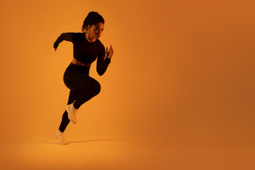 Determined fit lady running in mid-air, exercising during cardio workout over neon orange studio background, free space
