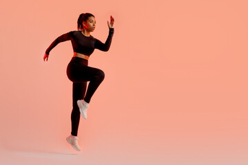Fototapeta na wymiar Sporty black lady jumping, having cardio training, wearing black fitwear, exercising over neon background, free space