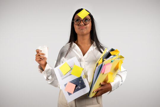 Busy tired young black business woman in glasses with many folders with cup coffee takeaway look at sticker on forehead