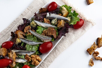 Salad featuring white Spanish anchovies on a bed of mixed greens with grape tomatoes, blue cheese, sourdough croutons, and walnuts.