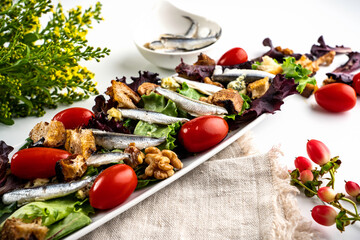 Salad featuring white Spanish anchovies on a bed of mixed greens with grape tomatoes, blue cheese, sourdough croutons, and walnuts.