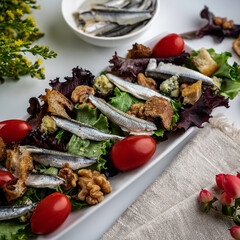 Salad featuring white Spanish anchovies on a bed of mixed greens with grape tomatoes, blue cheese, sourdough croutons, and walnuts.
