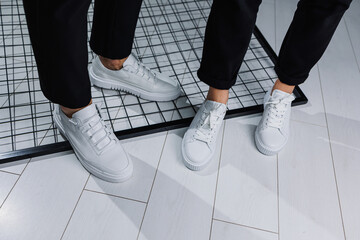Close-up of male and female legs in black pants and white casual sneakers. Summer men's and women's...