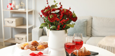 Vase with beautiful bouquet of flowers, pastries and glasses of wine for Valentine's Day celebration on dining table in room