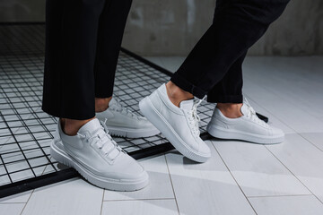 Close-up of male and female legs in black pants and white casual sneakers. Summer men's and women's leather shoes