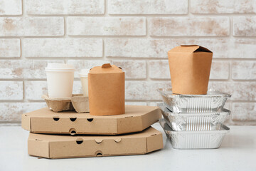 Set of food delivery containers on white table near light brick wall