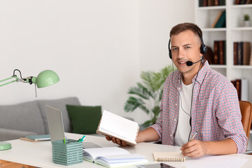 Fototapeta premium Young man with headset and notebook studying online at home