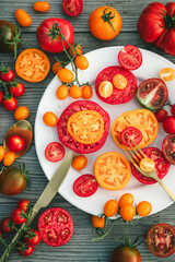 Delicious raw fresh colorful tomatoes on white round plate with fork and knife on wooden background. Chopped red and yellow tomatoes. Healthy food