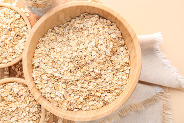 Wooden bowls of raw oatmeal on color background, closeup